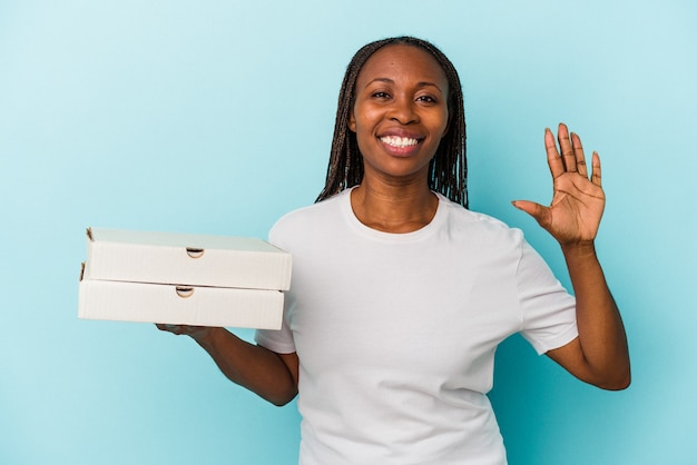 Jonge afro-amerikaanse vrouw met pizza's geïsoleerd op blauwe achtergrond glimlachend vrolijk nummer vijf met vingers.