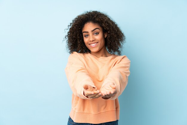 Jonge Afro-Amerikaanse vrouw op blauwe muur met lege ruimte denkbeeldige op de palm om een advertentie in te voegen