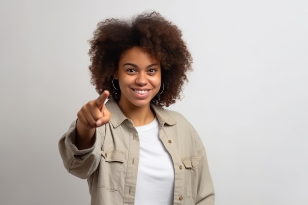 Jonge Afro-Amerikaanse vrouw wijst met haar vinger naar de camera op een grijze achtergrond.