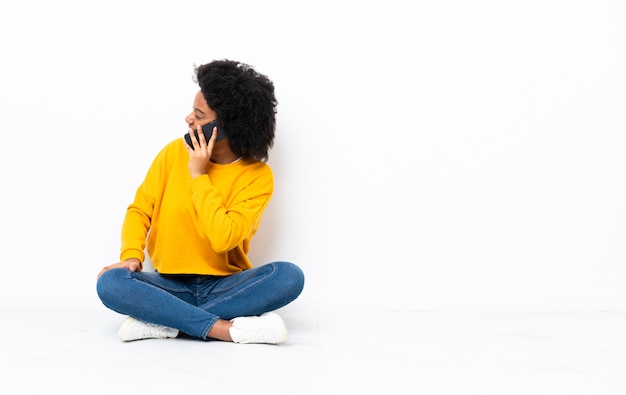 Jonge Afro-Amerikaanse vrouw zittend op de vloer houden een gesprek met de mobiele telefoon met iemand