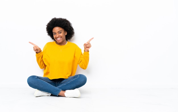 Jonge Afro-Amerikaanse vrouw, zittend op de vloer wijzende vinger naar de zijkanten en gelukkig