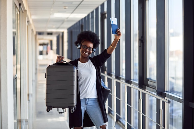 Jonge Afro-Amerikaanse vrouwelijke passagier in casual kleding en koptelefoon is op de luchthaven met bagage.