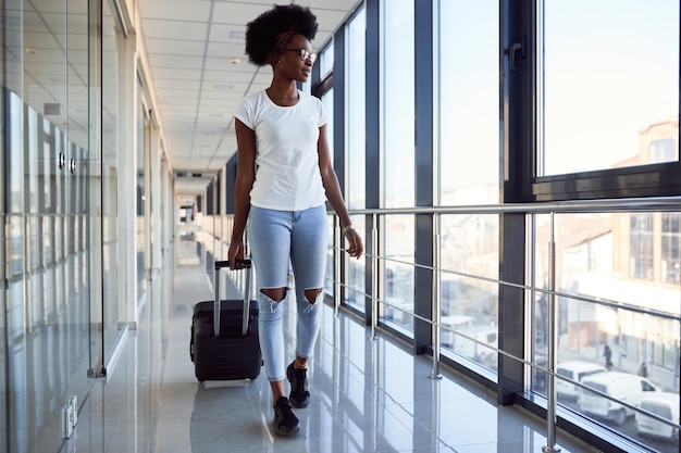 Jonge afro-amerikaanse vrouwelijke passagier in casual kleding is op de luchthaven met bagage.