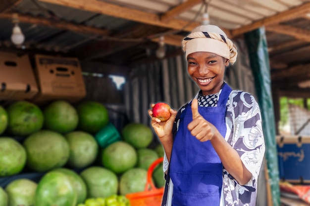 Foto jonge afro-amerikaanse vrouwelijke verkoper steekt de duim omhoog bij de fruitstand