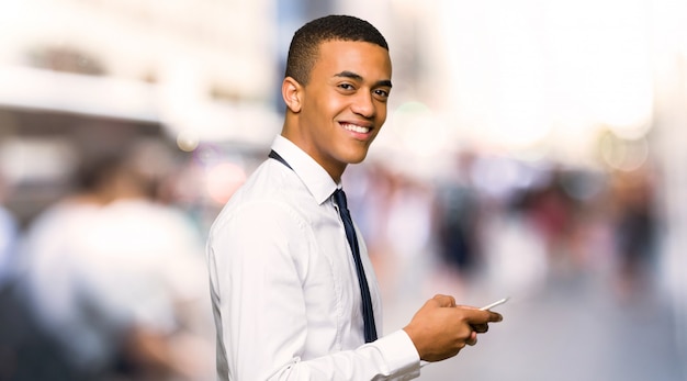 Jonge afro Amerikaanse zakenman die een bericht met mobiel in de stad verzendt