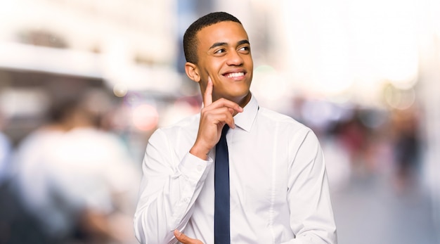 Jonge afro Amerikaanse zakenman die een idee denkt terwijl omhoog het kijken in de stad