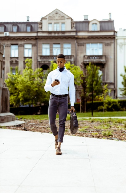 Jonge Afro-Amerikaanse zakenman die een mobiele telefoon gebruikt terwijl hij op straat loopt