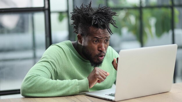 Jonge afro-amerikaanse zakenman zit in een loft-kantoor of café en werkt aan een nieuw online IT-opstartproject met behulp van een laptop