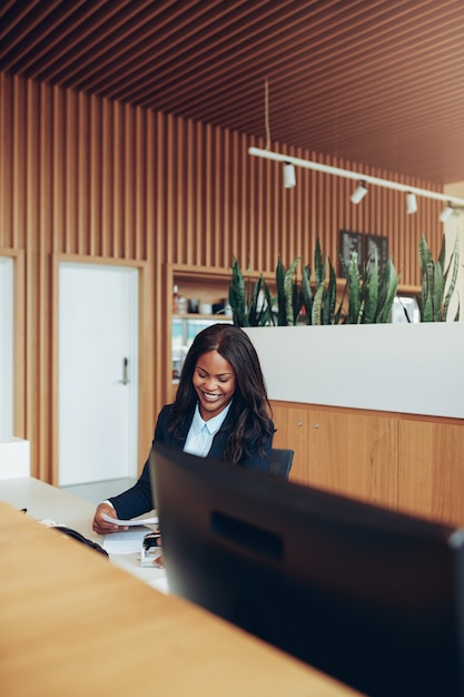 Jonge Afro-Amerikaanse zakenvrouw die lacht terwijl ze papierwerk doorneemt aan een bureau bij de receptie