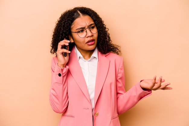 Jonge Afro-Amerikaanse zakenvrouw met mobiele telefoon geïsoleerd op beige background