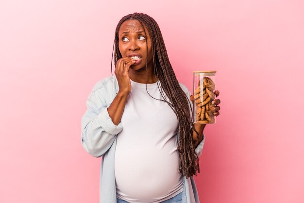 Jonge Afro-Amerikaanse zwangere vrouw met cookies geïsoleerd op roze achtergrond ontspannen denken over iets kijken naar een kopie ruimte.