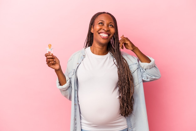 Jonge Afro-Amerikaanse zwangere vrouw met fopspeen geïsoleerd op roze achtergrond met een mobiel telefoongesprek gebaar met vingers.