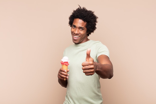 Jonge afro man die zich trots, zorgeloos, zelfverzekerd en gelukkig voelt, positief glimlacht met duimen omhoog