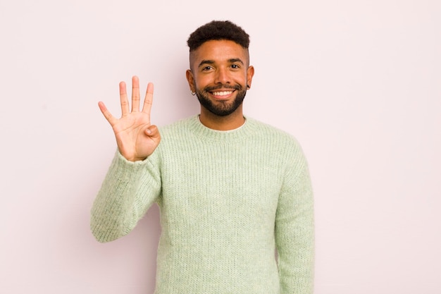 Jonge afro-man glimlacht en ziet er vriendelijk uit en toont nummer vier of vierde met de hand naar voren die aftelt