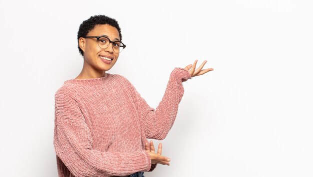 Jonge afro-vrouw die trots en zelfverzekerd glimlacht, zich gelukkig en tevreden voelt en een concept op kopieerruimte toont