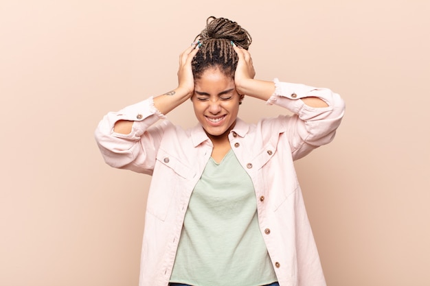 Foto jonge afro-vrouw die zich gestrest en gefrustreerd voelt, de handen opheft naar het hoofd, zich moe, ongelukkig en met migraine voelt