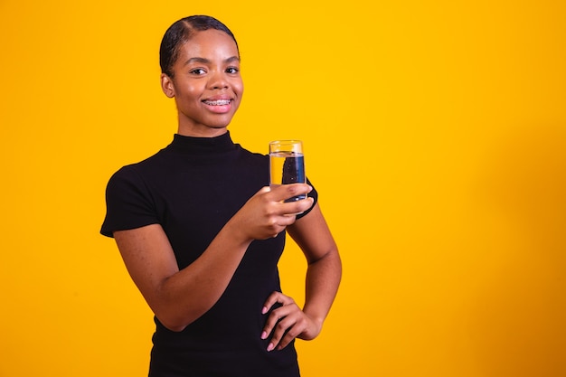 Jonge afro vrouw drinkwater op gele achtergrond. Jong meisje met glas water