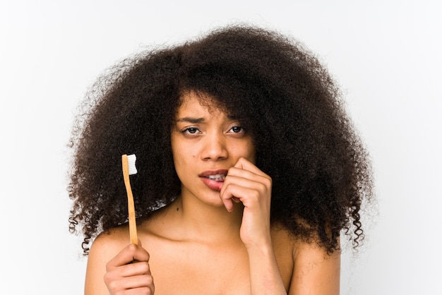 Jonge afro vrouw met een tandenborstel geïsoleerd bijten nagels, nerveus en erg angstig.