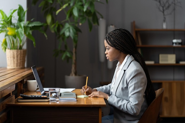 Jonge afro zakenvrouw stagiair werkt online op laptop en maakt aantekeningen voor zakelijk rapport op kantoor