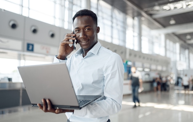 Jonge afrozakenman met laptop en telefoon in autotoonzaal. Succesvolle zakenman op motorshow, zwarte man in formele kleding