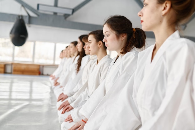 Jonge aikidostudenten die kimono dragen die in rij zitten. Sportende tienerkinderen die wachten op het begin van de groepsles of luisteren naar hun coach tijdens de training