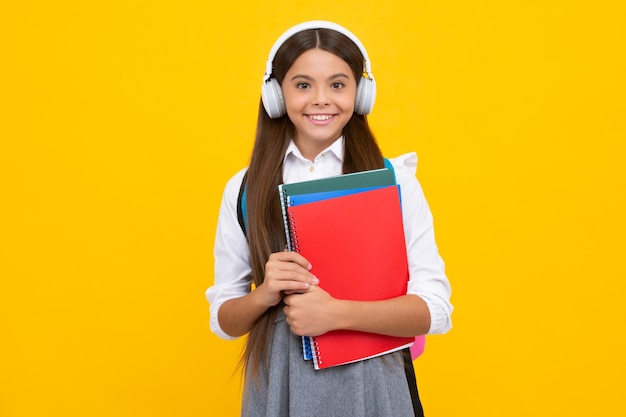 Jonge Amerikaanse meisje tiener student met koptelefoon en boeken geïsoleerd op gele achtergrond studio