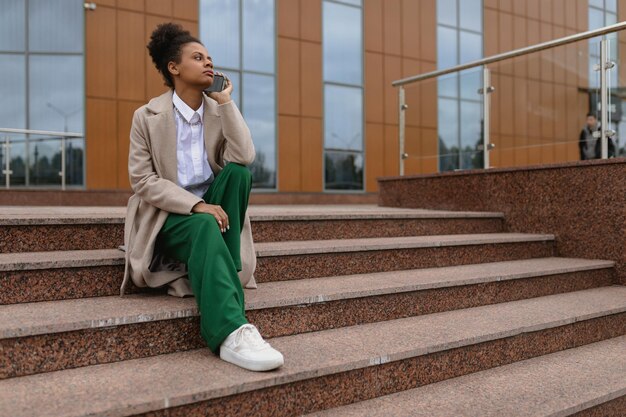 Jonge amerikaanse vrouwelijke freelance marketeer die aan de telefoon praat terwijl hij op de trappen van een zit