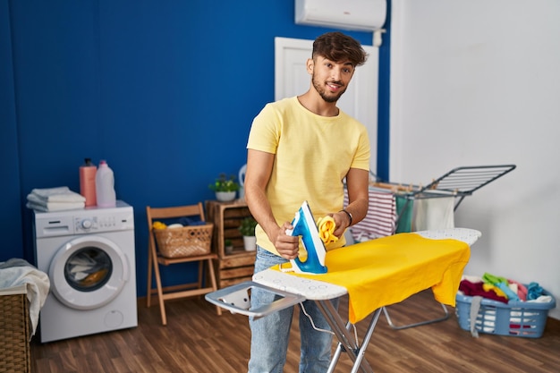 Jonge Arabier die zelfverzekerd glimlacht en kleding strijkt in de wasserette.