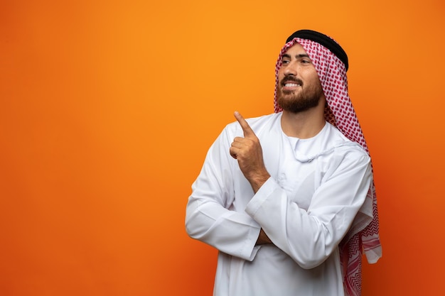 Jonge Arabier wijst met zijn hand naar ruimte op oranje achtergrond