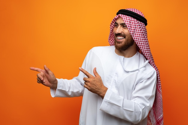 Jonge Arabier wijst met zijn hand naar ruimte op oranje achtergrond
