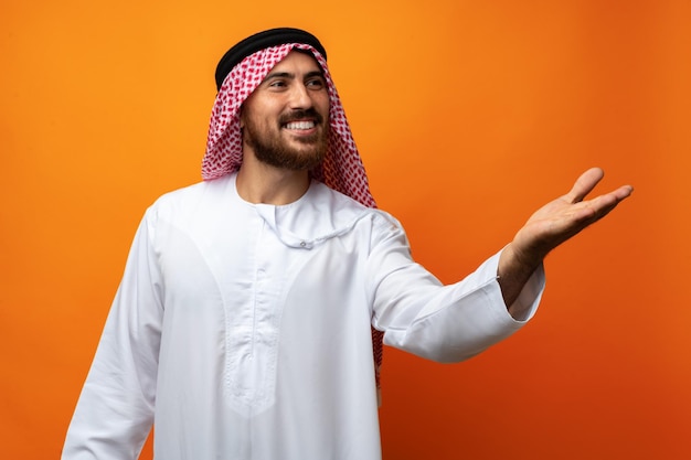 Jonge Arabier wijst met zijn hand naar ruimte op oranje achtergrond
