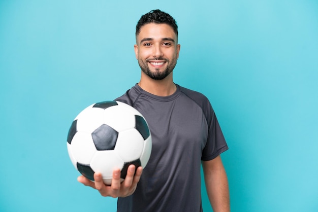 Jonge Arabische knappe man geïsoleerd op blauwe achtergrond met voetbal