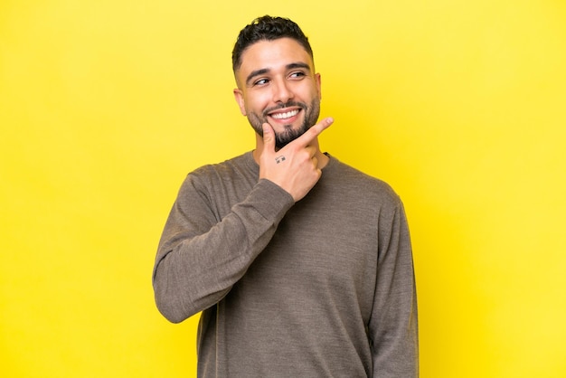 Jonge Arabische knappe man geïsoleerd op gele achtergrond die een idee denkt terwijl hij omhoog kijkt