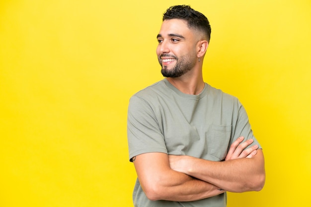 Jonge Arabische knappe man geïsoleerd op gele achtergrond opzij kijkend en glimlachend