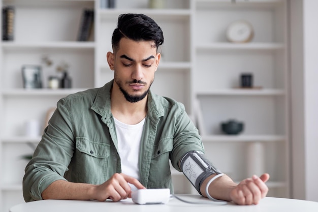 Jonge Arabische man die bloeddruk controleert met moderne tonometer thuis