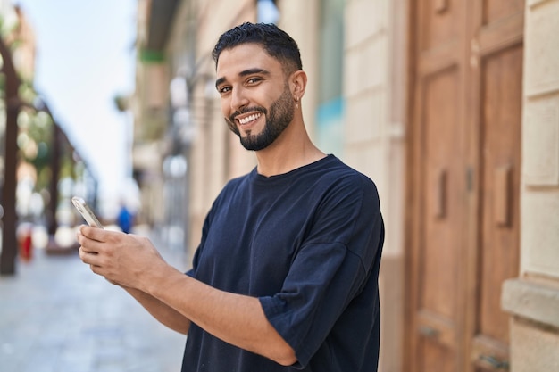 Jonge arabische man die lacht zelfverzekerd met behulp van smartphone op straat