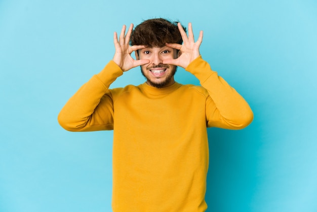 Jonge Arabische man die op blauwe achtergrond ogen openhouden om een succeskans te vinden.