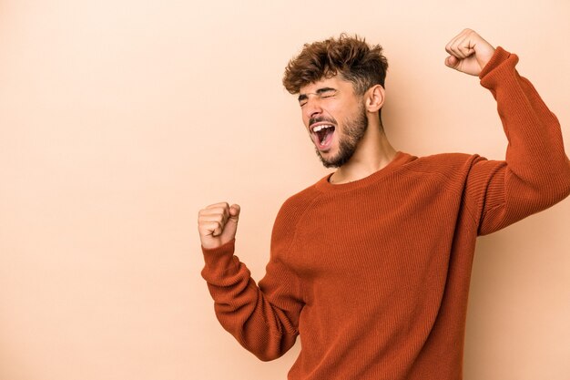 Jonge Arabische man geïsoleerd op beige achtergrond die vuist opheft na een overwinning, winnaar concept.