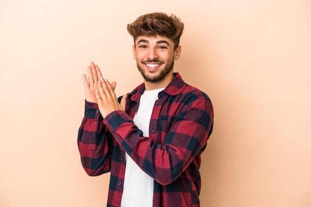 Jonge arabische man geïsoleerd op beige achtergrond voelt zich energiek en comfortabel, wrijft zelfverzekerd over de handen.