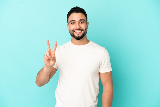 Jonge Arabische man geïsoleerd op blauwe achtergrond glimlachend en overwinning teken tonen
