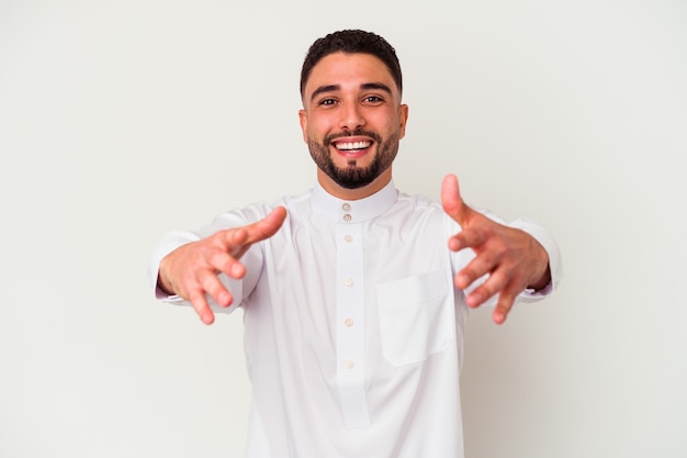 Jonge Arabische man in typische Arabische kleding geïsoleerd op een witte achtergrond voelt zich zelfverzekerd en geeft een knuffel aan de camera.