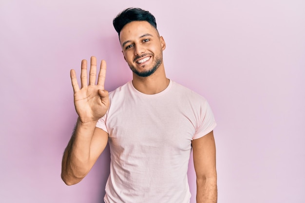 Jonge arabische man in vrijetijdskleding die met vingers nummer vier laat zien en omhoog wijst terwijl hij zelfverzekerd en gelukkig glimlacht