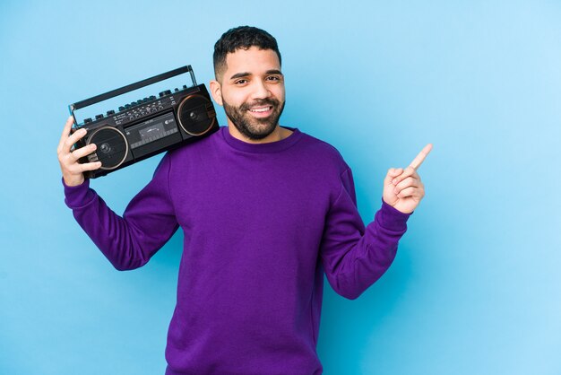 Jonge arabische man met een radiocassette geïsoleerd jonge arabische man luisteren muziek lacht en wijst opzij, iets op lege ruimte weer gegeven.