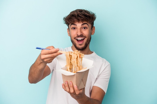 Jonge Arabische man met een take-away noedels geïsoleerd op blauwe achtergrond