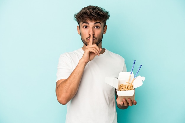 Jonge arabische man met een take-away noedels geïsoleerd op een blauwe achtergrond die een geheim houdt of om stilte vraagt.