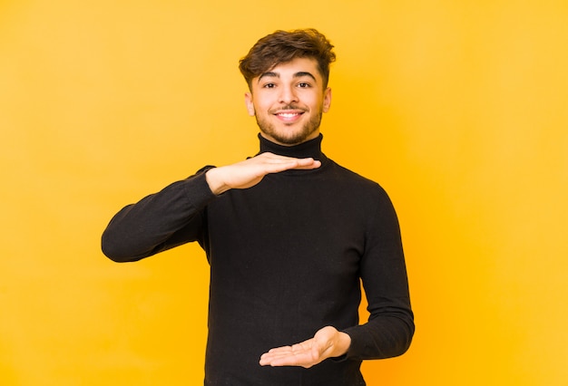 Jonge arabische man op een gele muur met iets met beide handen