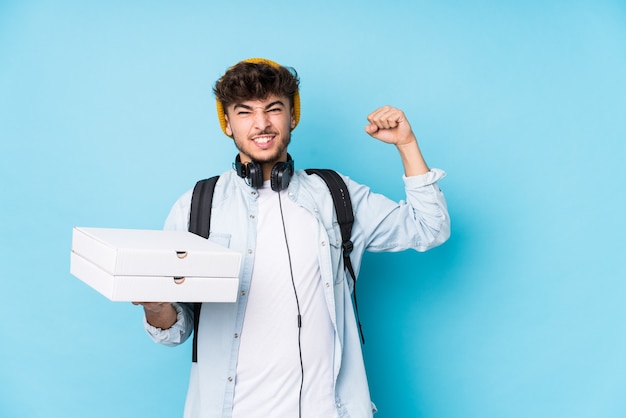 Jonge arabische student man met pizza's geïsoleerd verhogen vuist na een overwinning, winnaar concept.