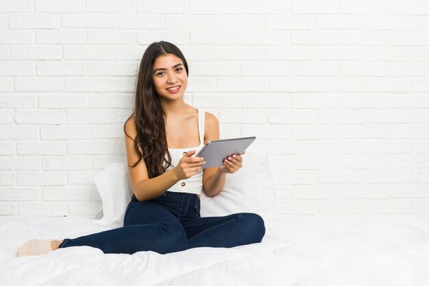 Jonge Arabische vrouw die met haar laptop aan het gelukkig, glimlachende en vrolijke bed werkt.