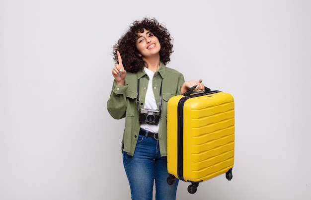 Jonge arabische vrouw die vriendelijk glimlacht en kijkt, nummer één of eerst met vooruit hand toont, reisconcept aftelt