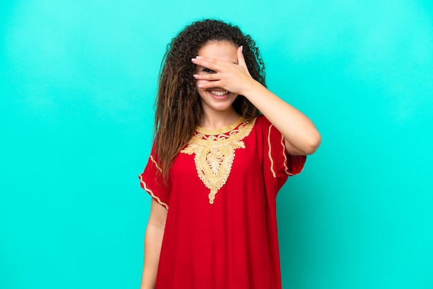 Jonge Arabische vrouw geïsoleerd op blauwe achtergrond die haar ogen met haar handen bedekt en glimlacht